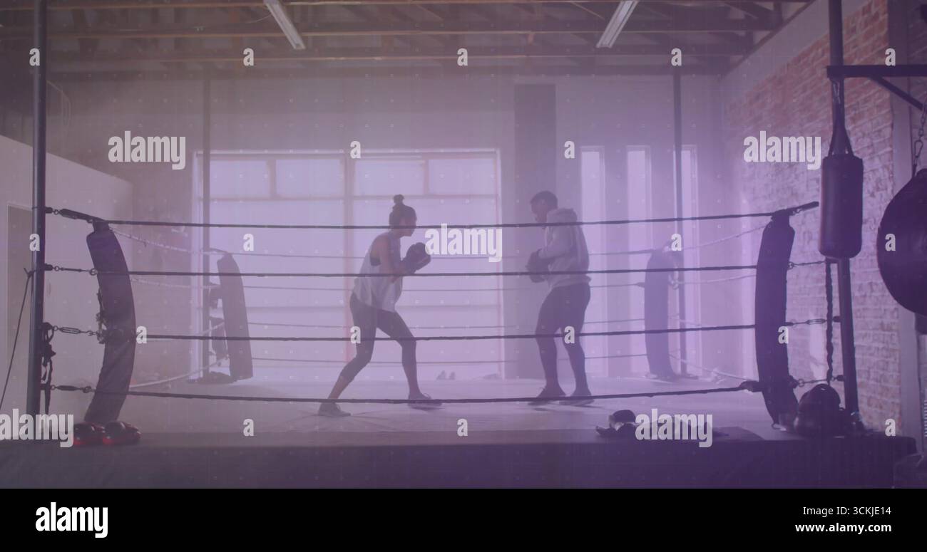 Sparring per gli apprendisti con guanti che si scambiano i jab nell'anello della palestra del magazzino, con sacchetti perforati e impacchi a mano Foto Stock