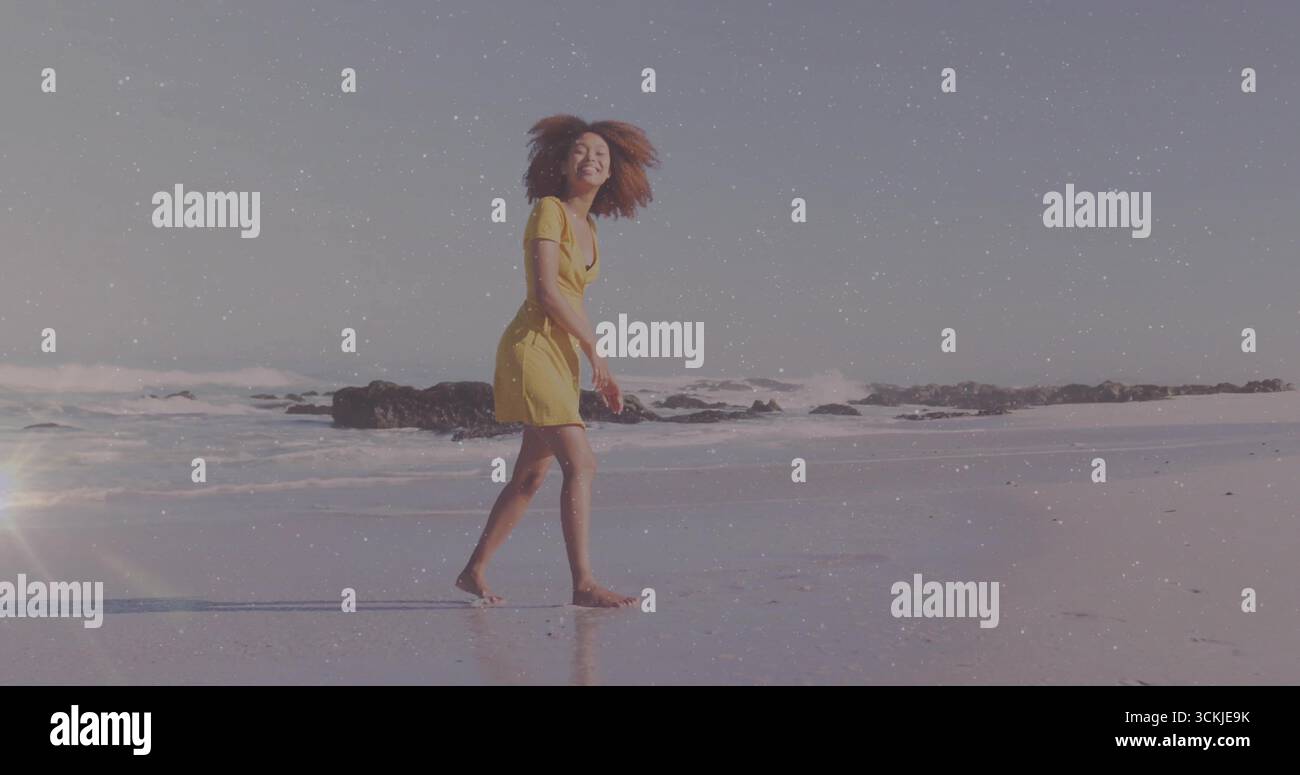 Donna che cammina con un abito estivo giallo passeggiando sulla spiaggia bagnata, rocce vulcaniche e onde dolci Foto Stock