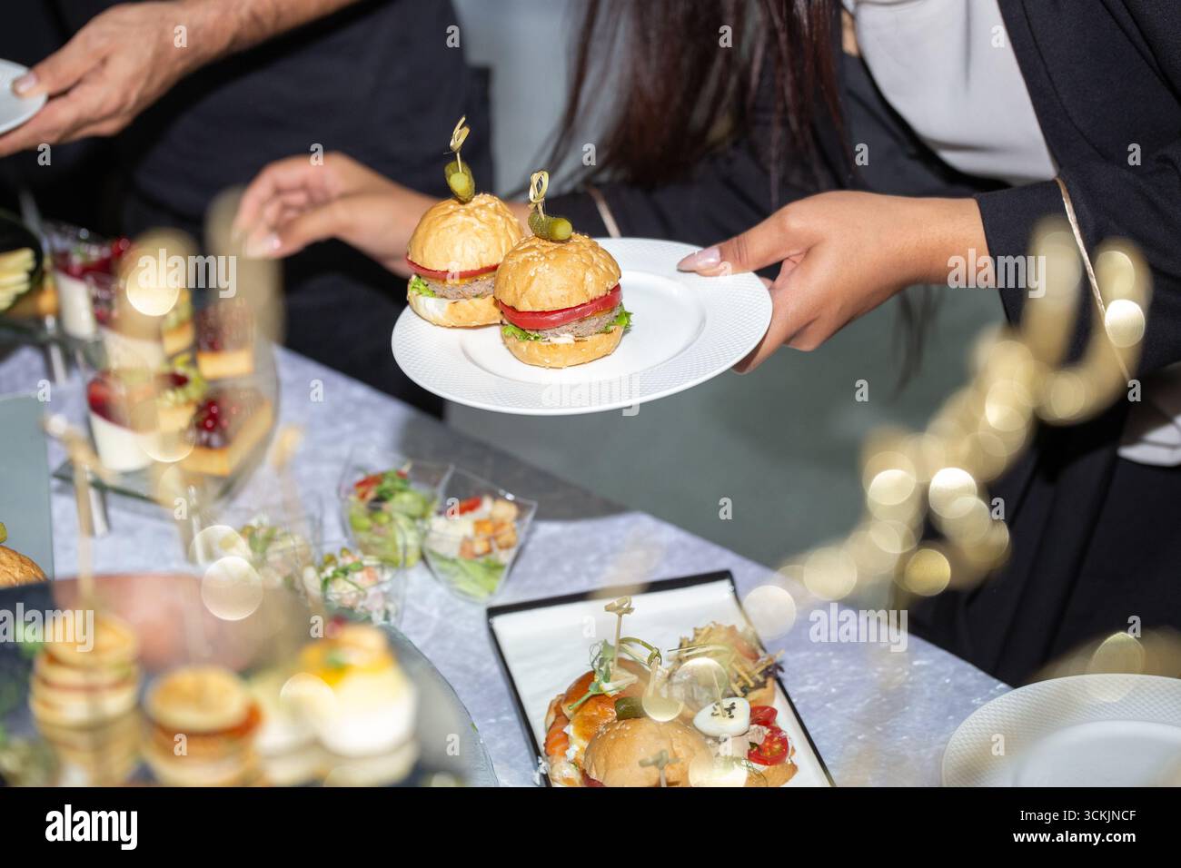 Una donna che gusta eleganti tartine su un tavolo festivo con tè, vino e decorazioni floreali. Atmosfera sofisticata per una cena formale o un ricevimento di nozze Foto Stock