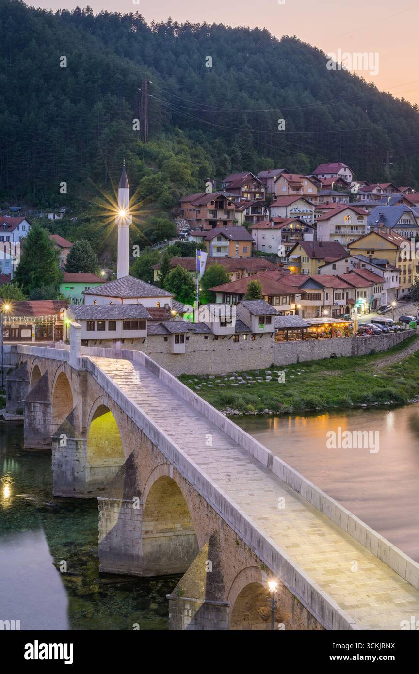 Konjic al crepuscolo con edifici illuminati, il vecchio ponte e riflessi sulla superficie del fiume. Foto Stock
