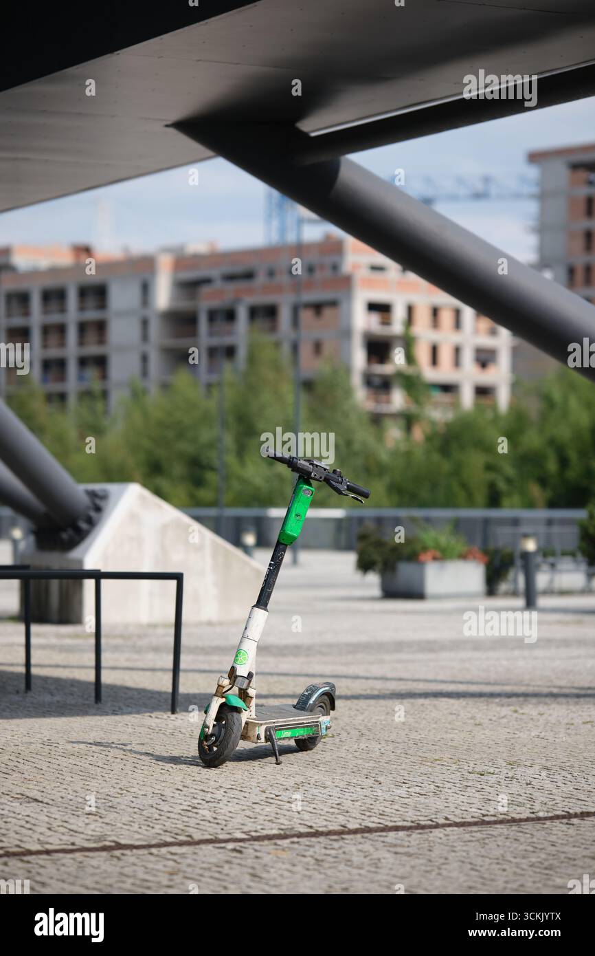Lodz, Polonia - 6 luglio 2025: Scooter elettrico calce parcheggiato sul marciapiede in città con edifici moderni sullo sfondo Foto Stock