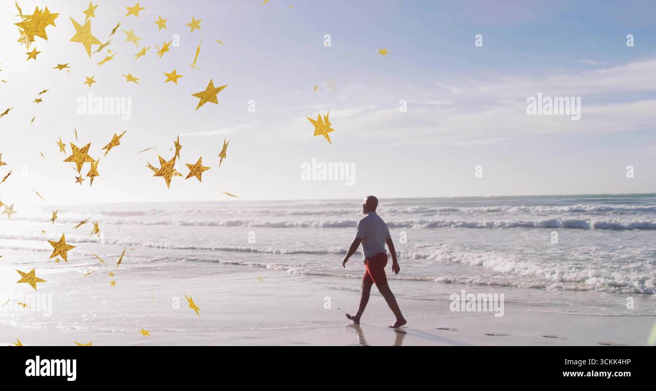 Uomo maturo in maglietta bianca e pantaloncini rossi lungo il litorale bagnato, con coriandoli dorati Foto Stock