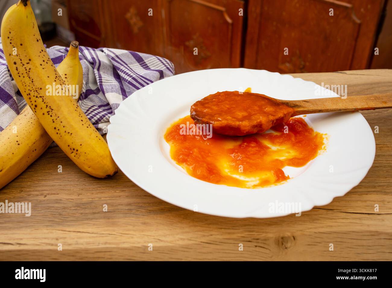 Marmellata di banana di colore arancio con curcuma in un cucchiaio di legno pieno , su un piatto bianco, fuoco morbido Foto Stock