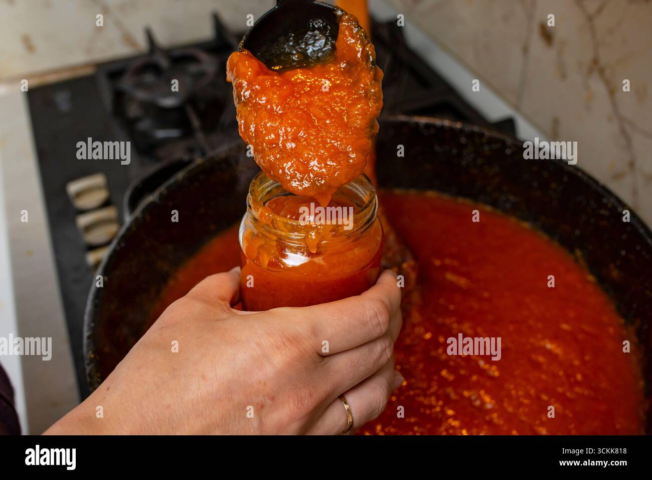 Mani di donna che porgono marmellata calda di albicocca o pesca in un vaso di vetro, con messa a fuoco morbida Foto Stock