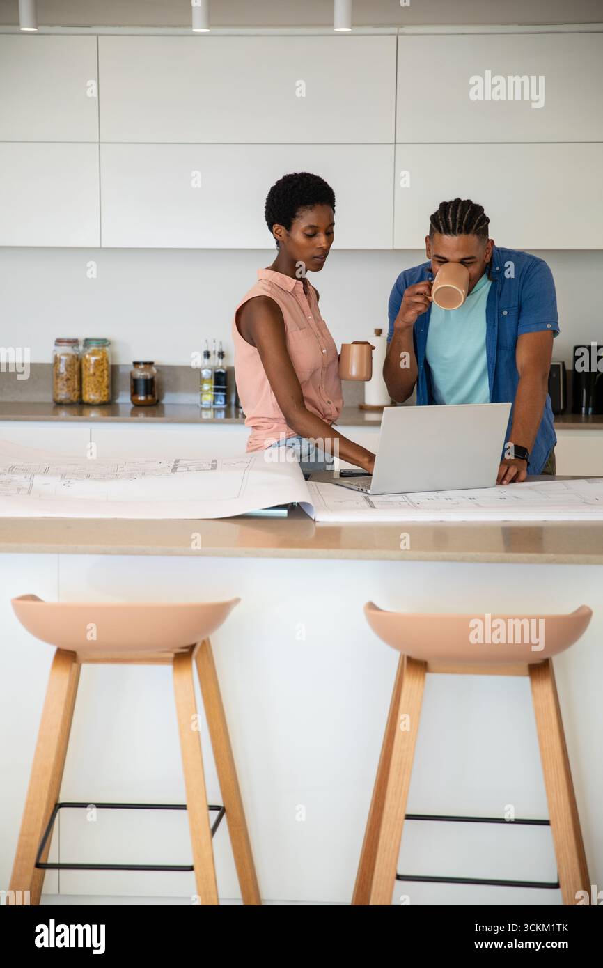 Diverse coppie che collaborano in cucina sull'isola con computer portatile in argento e tazze in ceramica Foto Stock