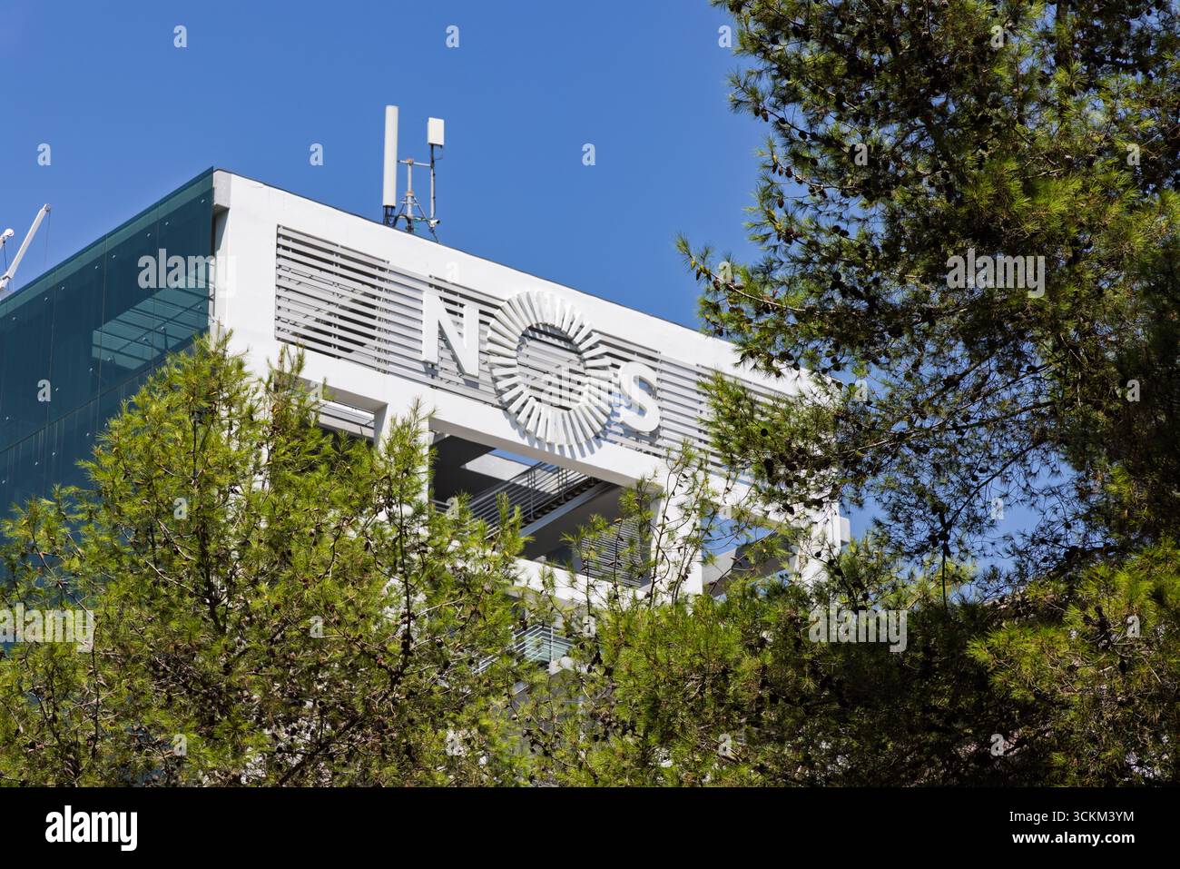 Una foto ravvicinata della facciata bianca simile a una griglia di un edificio moderno con il logo NOS, adagiata su un cielo blu brillante. Lisbona, Portogallo. Agosto 2025. Foto Stock