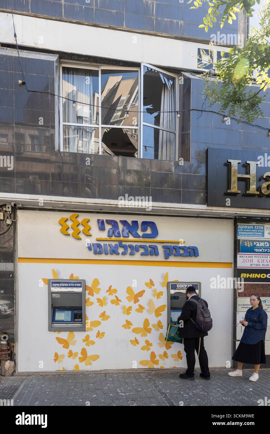Haifa, Israele, 11 giugno 2025, un ebreo ortodosso al bancomat. Finestre rotte di un edificio dopo che un missile iraniano ha colpito. Foto Stock