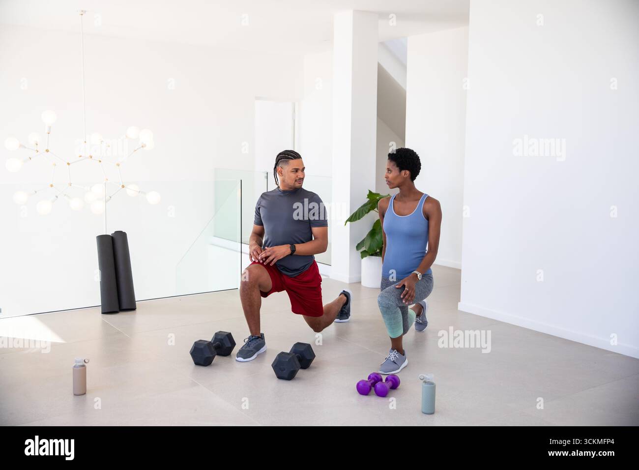 Diversi partner di allenamento che indossano abbigliamento atletico per fare affondamenti in palestra con manubri Foto Stock