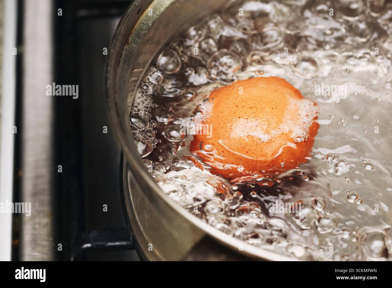 Uovo bollito in una pentola con acqua calda. Cucinare la colazione in cucina. Preparazione di uova di pollo fresche per alimenti sani. Processo culinario con acqua a bolle d'aria. Foto Stock