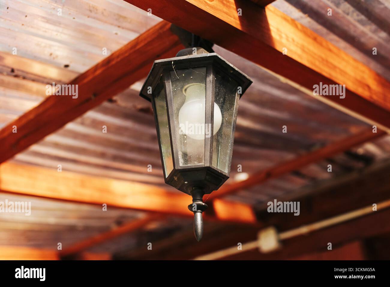 Lampada da esterno appesa sotto il tetto di legno. Dettagli rustici della lampada. Primo piano degli elementi di illuminazione esterni vintage. Oggetto architettonico tradizionale per la casa. Foto Stock