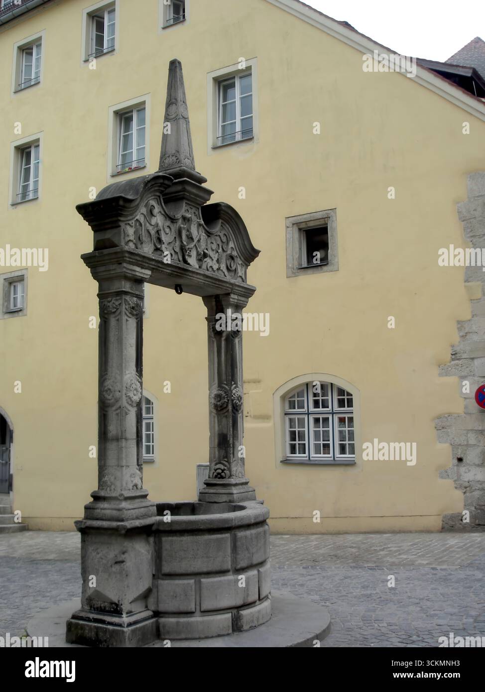 Una vista accattivante della fontana WidfangBrunnen, che mostra intricati lavori in pietra circondati da edifici storici a Ratisbona, evocando il fascino di Foto Stock
