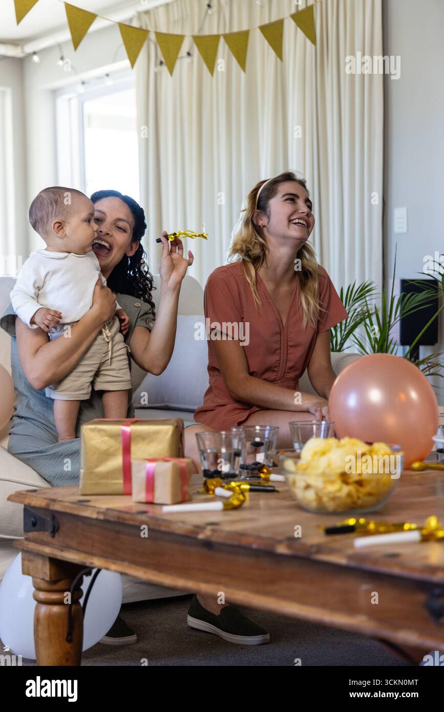 Diverse donne e bambini che giocano a corno dorato sul divano in soggiorno con regali Foto Stock