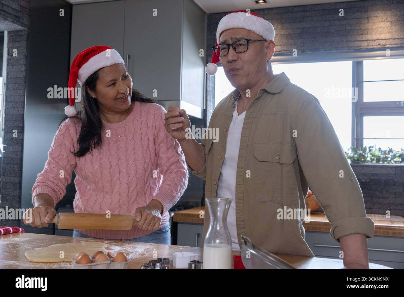 Una coppia di cappelli di babbo natale preparava l'impasto al bancone della cucina con il mattarello e le uova Foto Stock