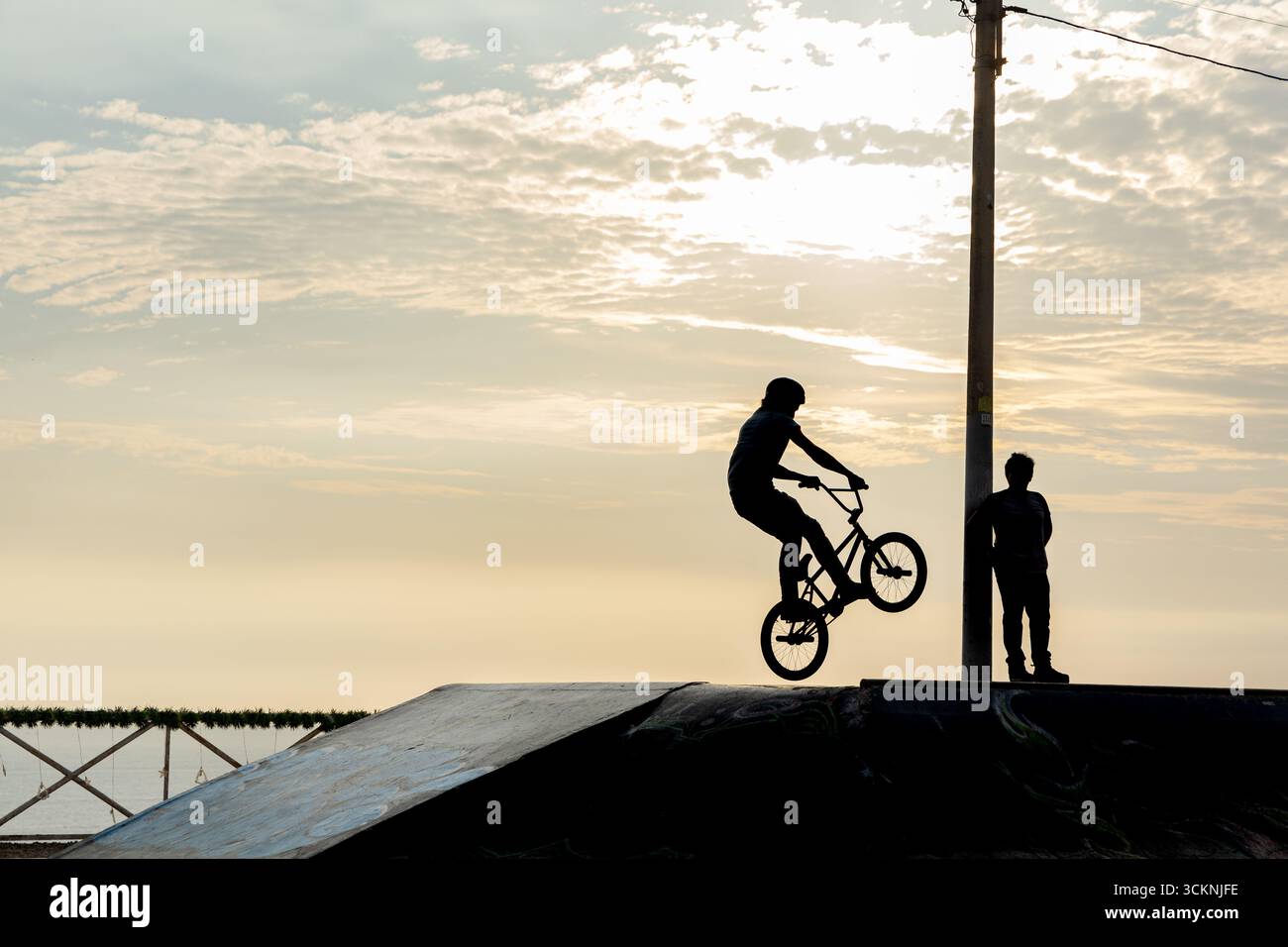 Ciclista freestyle che pratica il BMX su strada in retroilluminazione al tramonto Foto Stock