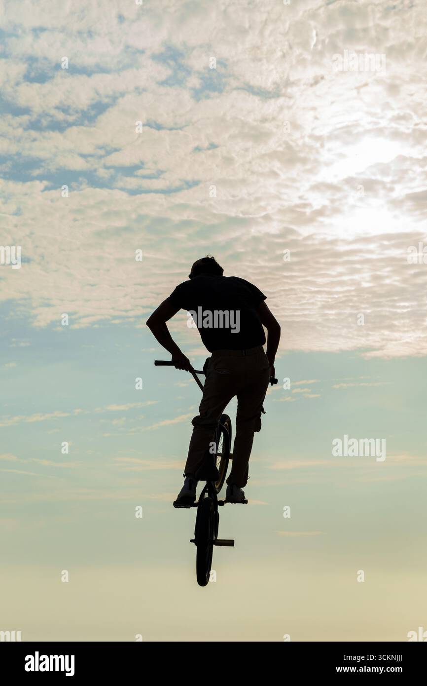 Ciclista freestyle che pratica il BMX su strada in retroilluminazione al tramonto Foto Stock