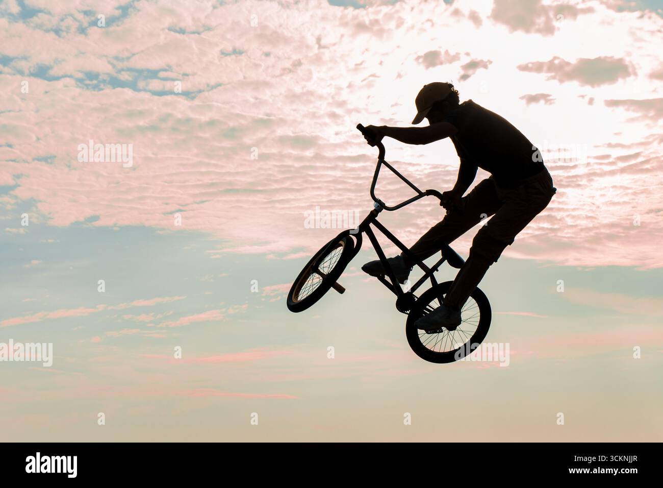 Ciclista freestyle che pratica il BMX su strada in retroilluminazione al tramonto Foto Stock