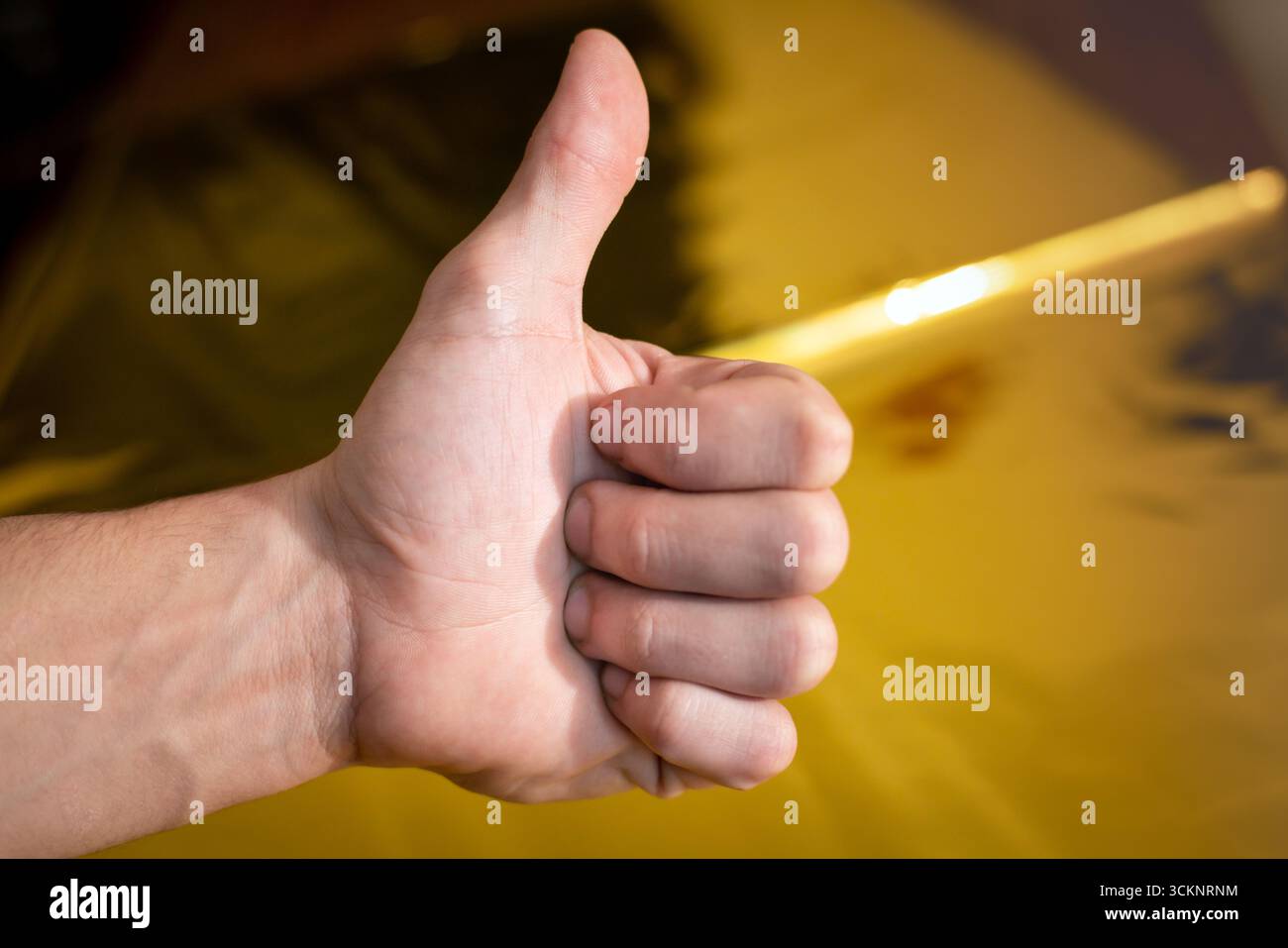 Primo piano di una mano che mostra un segno con i pollici su uno sfondo dorato lucido. Foto Stock