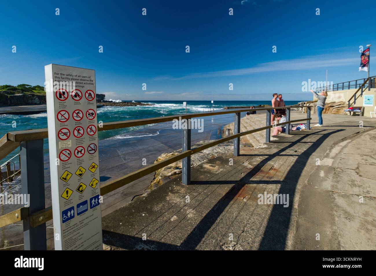Cartello con le linee guida di sicurezza vicino a un sentiero sul mare con persone che si godono il paesaggio costiero e la luce del sole, Clovelly Bay, Clovelly, Sydney Foto Stock