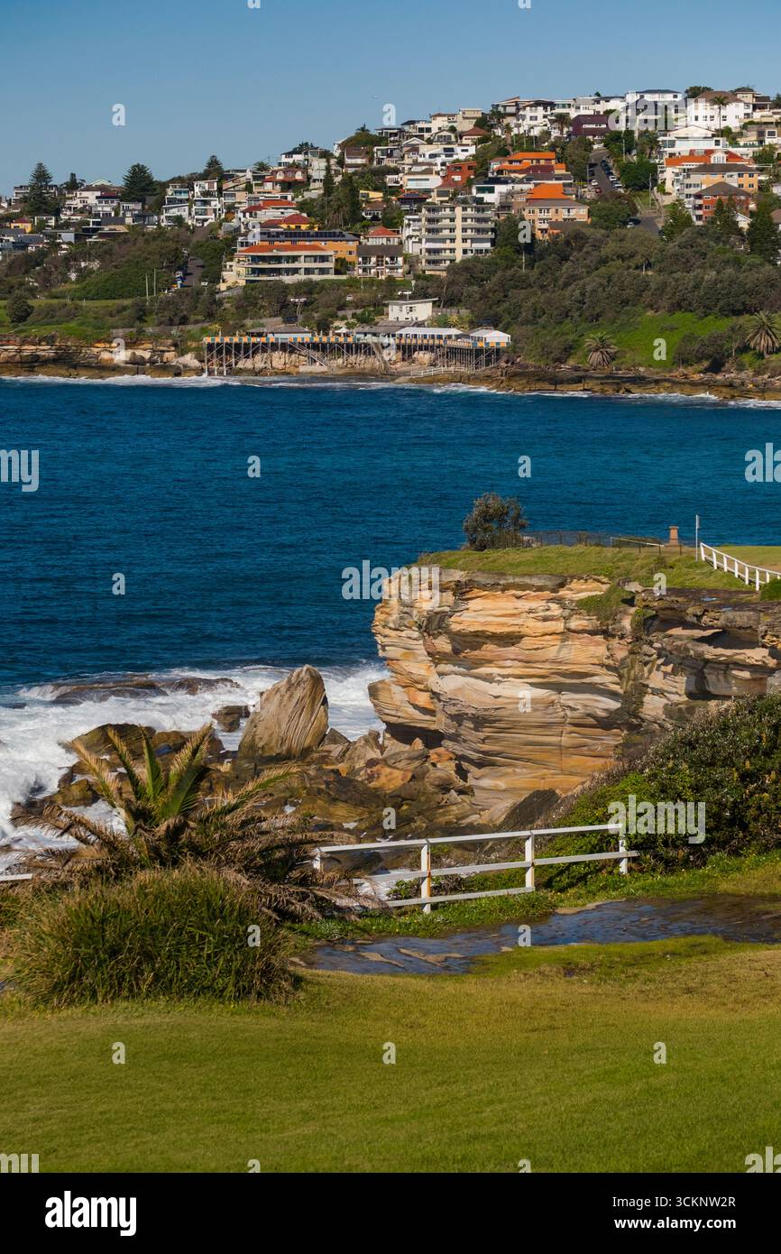 Una vista panoramica di un sentiero sulla scogliera vicino all'Oceano Pacifico, vegetazione lussureggiante e case residenziali che adornano le colline costiere sotto il cielo limpido Foto Stock