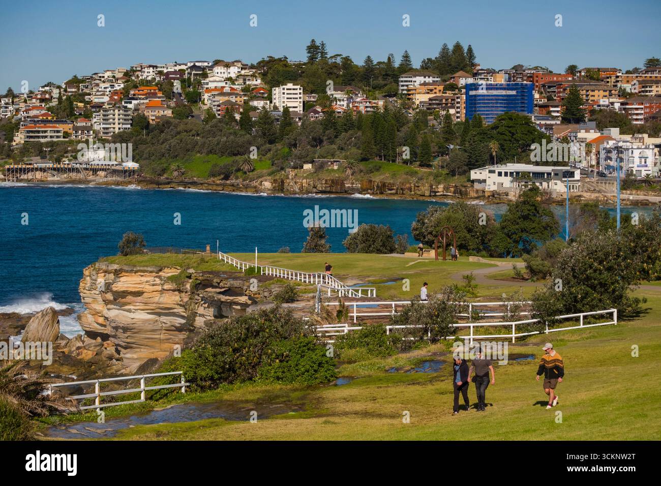 Un'area costiera panoramica con scogliere, un parco, case incantevoli e un oceano blu brillante. Le persone si godono piacevoli passeggiate, circondate dalla natura Foto Stock