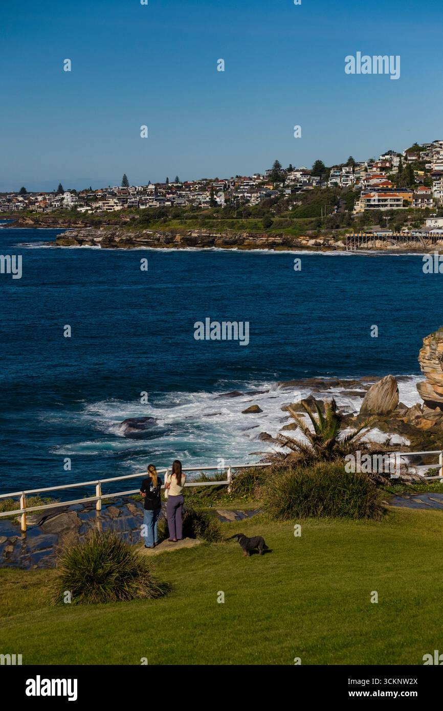 Foto panoramica della costa con due persone e un cane che si affaccia sul mare con affascinanti case in lontananza, che mostrano una serena e pittoresca Foto Stock