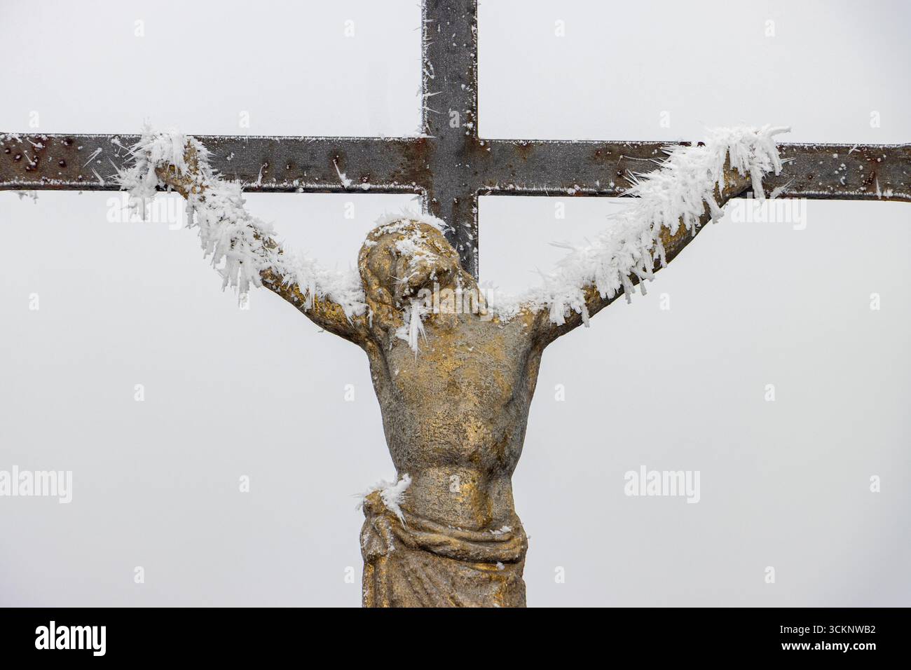 Un crocifisso invernale con gelo su sfondo nebbioso evoca temi di fede, sofferenza e perseveranza. Foto Stock