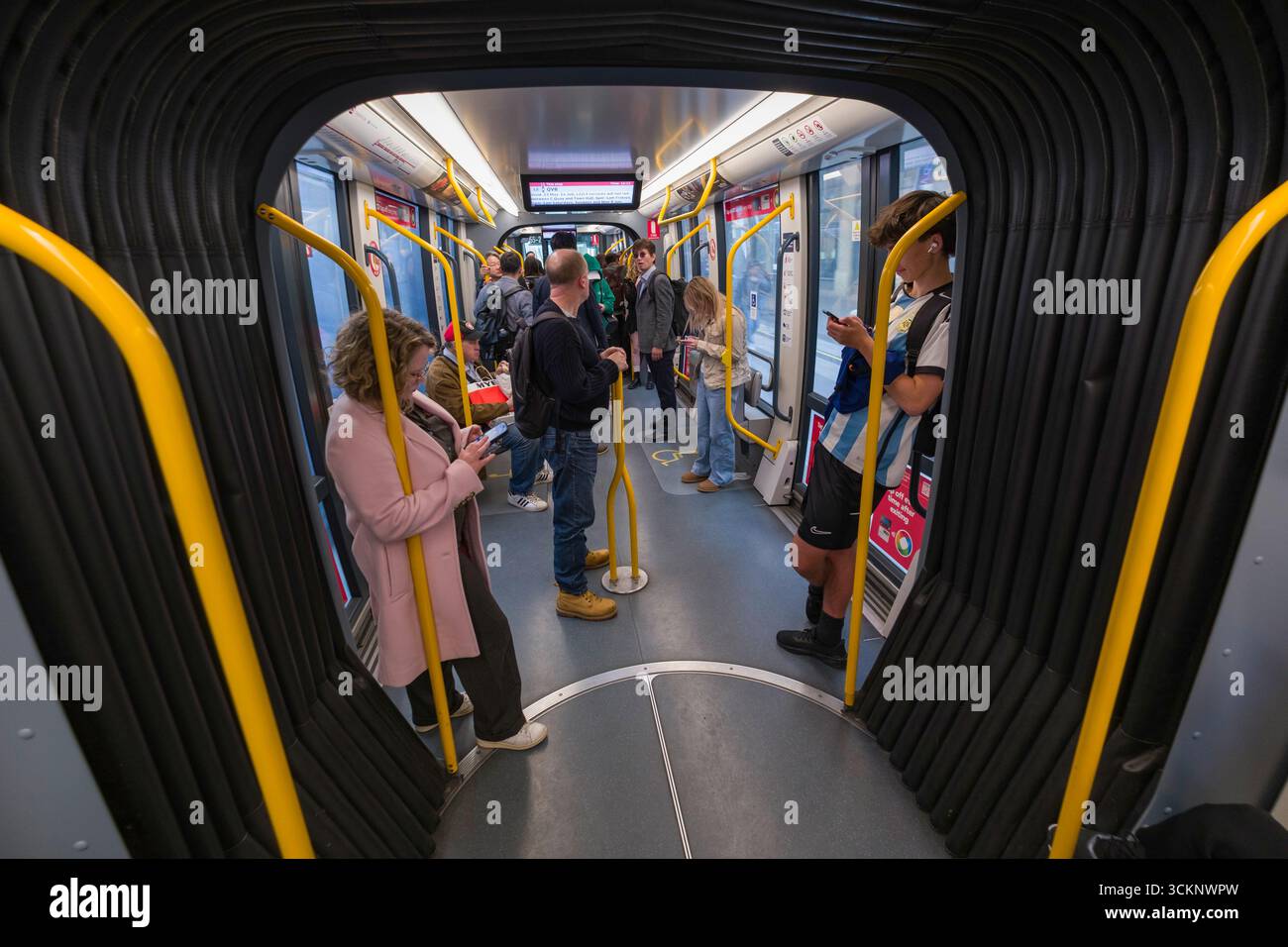 Un gruppo eterogeneo di persone si trova all'interno del Sydney Light Rail Train, interagendo con i propri smartphone. L'ambiente mette in risalto gli spostamenti urbani e i Foto Stock