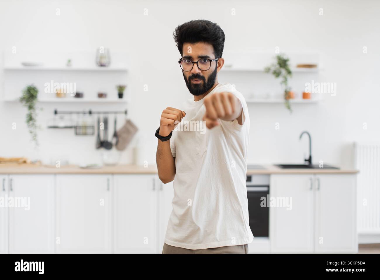 Uomo che pratica tecniche di pugilato in cucina con determinazione Foto Stock