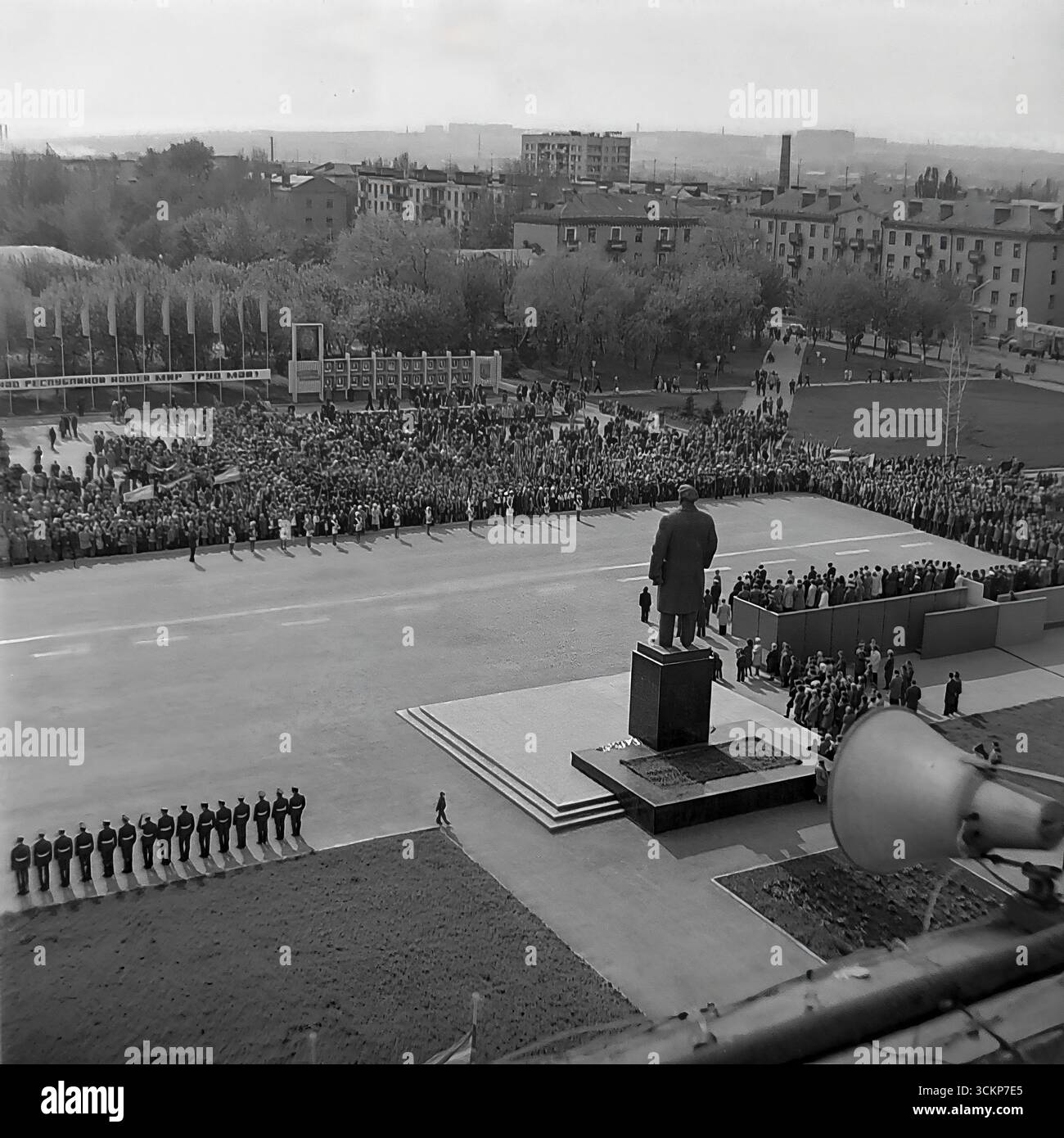 Una dimostrazione su larga scala del giorno di maggio in Piazza della Rivoluzione d'ottobre (ora Piazza Soborna) a Sloviansk, 1970 Migliaia di lavoratori con bandiere e una 'pace! Travaglio! Maggio!" Striscione marciano oltre la tribuna con la leadership e il monumento Lenin. Questo scatto è un vivido documento di un rituale di stato sovietico dell'era della stagnazione e un simbolo della vita collettiva e pacifica nel Donbas, molto prima dei tragici eventi futuri Foto Stock