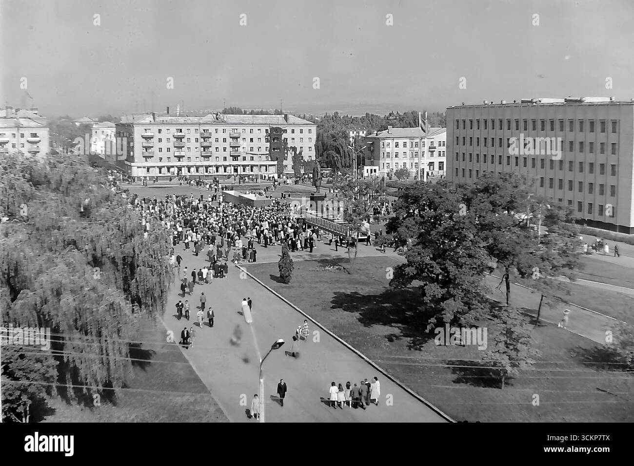 Viste panoramiche della piazza centrale della Rivoluzione d'ottobre (ora piazza Soborna) a Sloviansk, 1976, durante una grande festa pubblica. Migliaia di cittadini sono visti rilassarsi e passeggiare attraverso la piazza verdeggiante sullo sfondo di edifici amministrativi e residenziali. Questi scatti sono un potente simbolo della vita sociale pacifica, ordinata e vibrante nel Donbas durante l'era della stagnazione, catturando lo spirito della comunità della città molto prima dei tragici eventi che hanno distrutto questa esistenza idilliaca Foto Stock