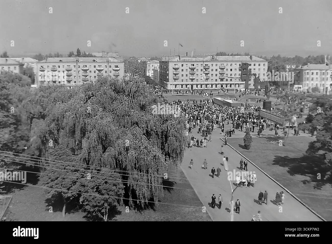 Viste panoramiche della piazza centrale della Rivoluzione d'ottobre (ora piazza Soborna) a Sloviansk, 1976, durante una grande festa pubblica. Migliaia di cittadini sono visti rilassarsi e passeggiare attraverso la piazza verdeggiante sullo sfondo di edifici amministrativi e residenziali. Questi scatti sono un potente simbolo della vita sociale pacifica, ordinata e vibrante nel Donbas durante l'era della stagnazione, catturando lo spirito della comunità della città molto prima dei tragici eventi che hanno distrutto questa esistenza idilliaca Foto Stock