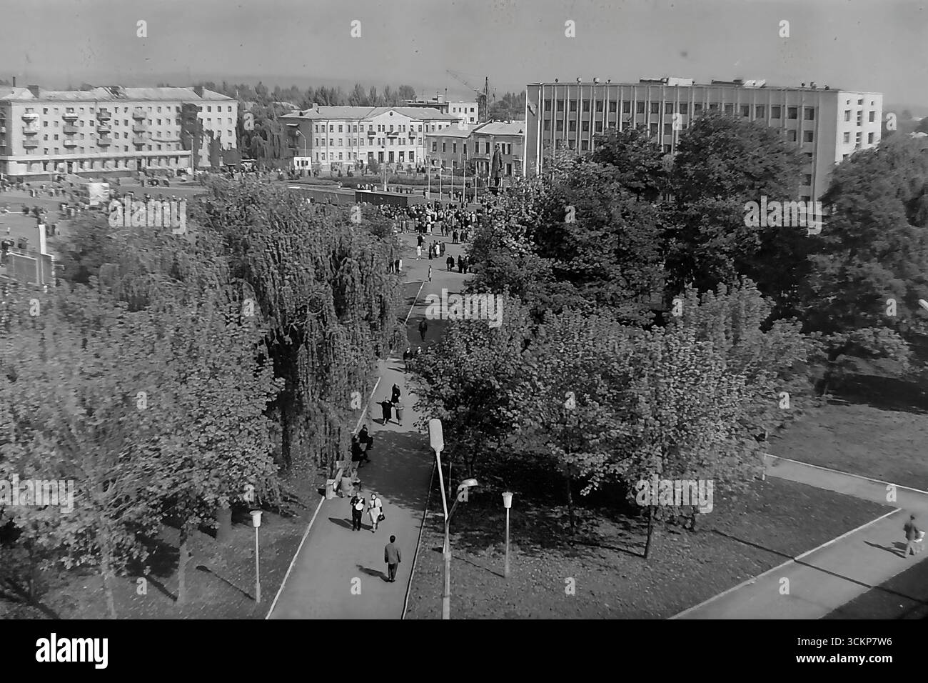 Viste panoramiche della piazza centrale della Rivoluzione d'ottobre (ora piazza Soborna) a Sloviansk, 1976, durante una grande festa pubblica. Migliaia di cittadini sono visti rilassarsi e passeggiare attraverso la piazza verdeggiante sullo sfondo di edifici amministrativi e residenziali. Questi scatti sono un potente simbolo della vita sociale pacifica, ordinata e vibrante nel Donbas durante l'era della stagnazione, catturando lo spirito della comunità della città molto prima dei tragici eventi che hanno distrutto questa esistenza idilliaca Foto Stock