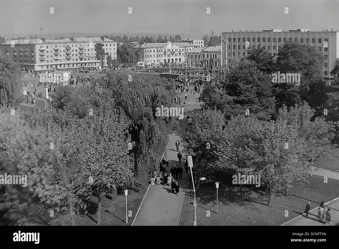 Viste panoramiche della piazza centrale della Rivoluzione d'ottobre (ora piazza Soborna) a Sloviansk, 1976, durante una grande festa pubblica. Migliaia di cittadini sono visti rilassarsi e passeggiare attraverso la piazza verdeggiante sullo sfondo di edifici amministrativi e residenziali. Questi scatti sono un potente simbolo della vita sociale pacifica, ordinata e vibrante nel Donbas durante l'era della stagnazione, catturando lo spirito della comunità della città molto prima dei tragici eventi che hanno distrutto questa esistenza idilliaca Foto Stock