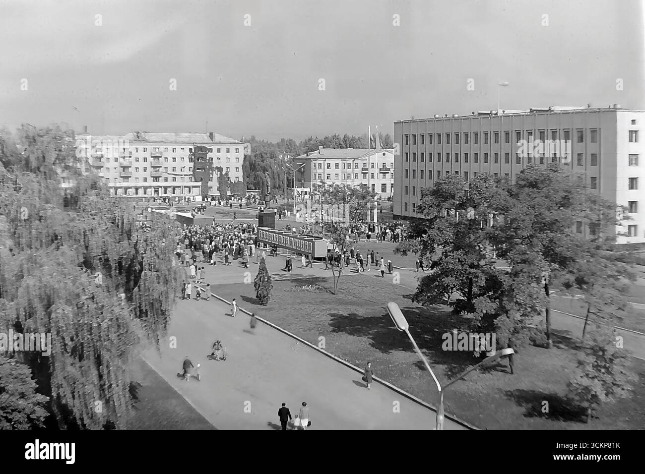 Viste panoramiche della piazza centrale della Rivoluzione d'ottobre (ora piazza Soborna) a Sloviansk, 1976, durante una grande festa pubblica. Migliaia di cittadini sono visti rilassarsi e passeggiare attraverso la piazza verdeggiante sullo sfondo di edifici amministrativi e residenziali. Questi scatti sono un potente simbolo della vita sociale pacifica, ordinata e vibrante nel Donbas durante l'era della stagnazione, catturando lo spirito della comunità della città molto prima dei tragici eventi che hanno distrutto questa esistenza idilliaca Foto Stock