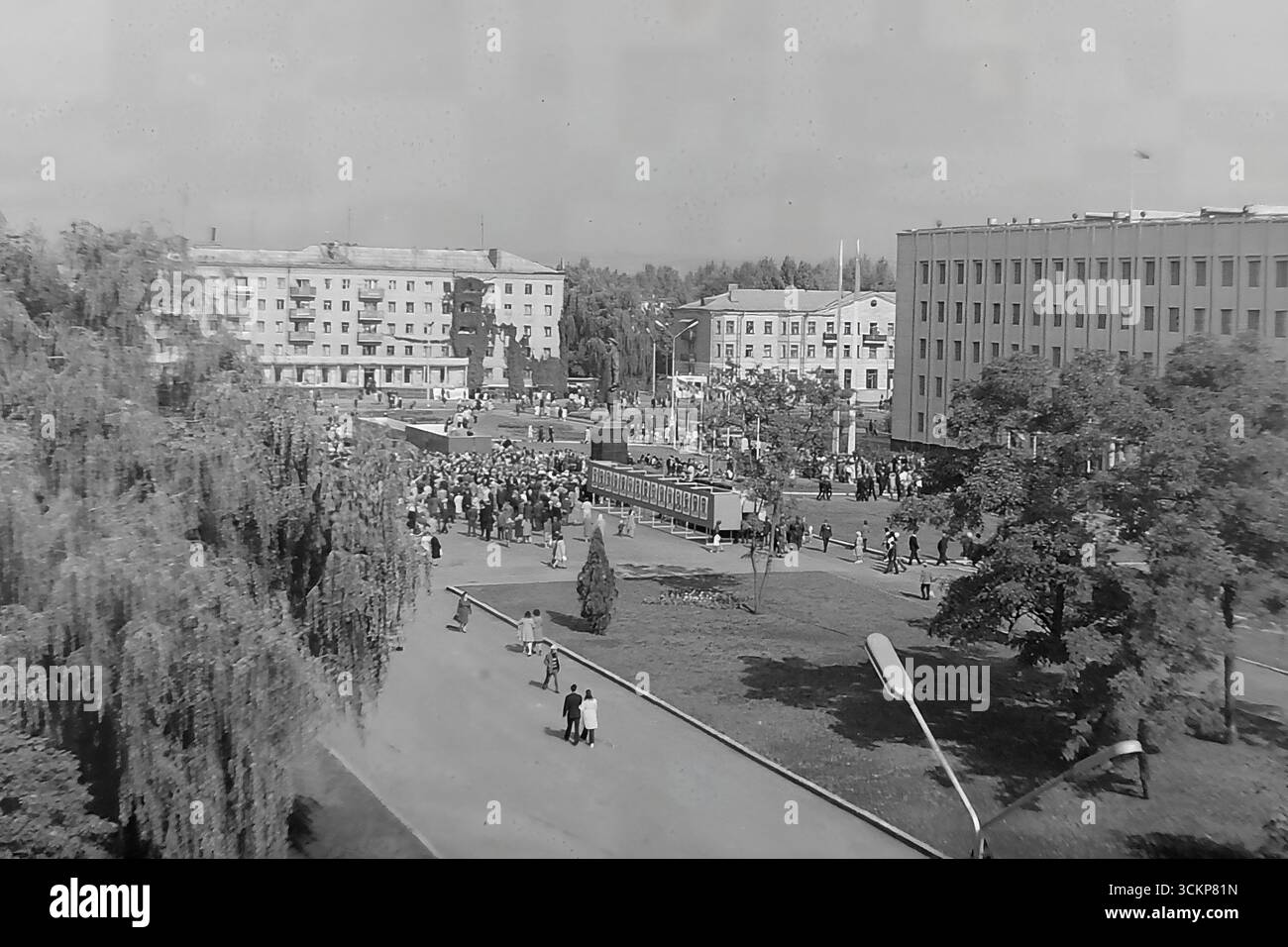 Viste panoramiche della piazza centrale della Rivoluzione d'ottobre (ora piazza Soborna) a Sloviansk, 1976, durante una grande festa pubblica. Migliaia di cittadini sono visti rilassarsi e passeggiare attraverso la piazza verdeggiante sullo sfondo di edifici amministrativi e residenziali. Questi scatti sono un potente simbolo della vita sociale pacifica, ordinata e vibrante nel Donbas durante l'era della stagnazione, catturando lo spirito della comunità della città molto prima dei tragici eventi che hanno distrutto questa esistenza idilliaca Foto Stock