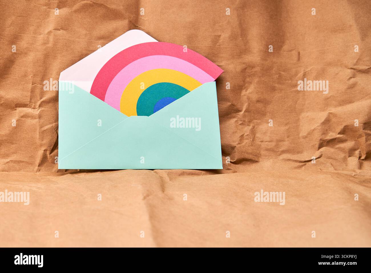 Busta verde con una carta a forma di arcobaleno su sfondo testurizzato di cartone. Foto Stock