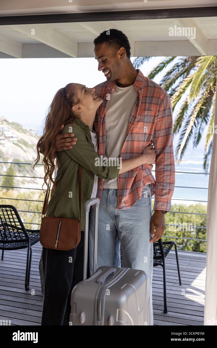 Diverse coppie che si abbracciano vicino alla ringhiera sul balcone coperto con vista sull'oceano e valigia con ruote Foto Stock