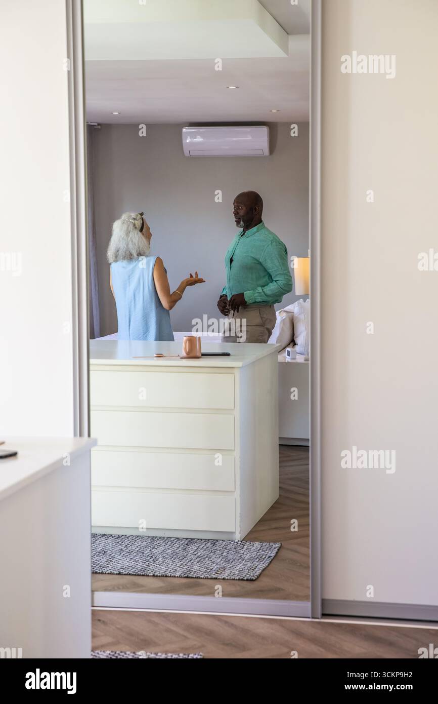 Diverse coppie anziane in piedi di fronte allo specchio a figura intera nella camera da letto dietro comò con tazza di rame Foto Stock