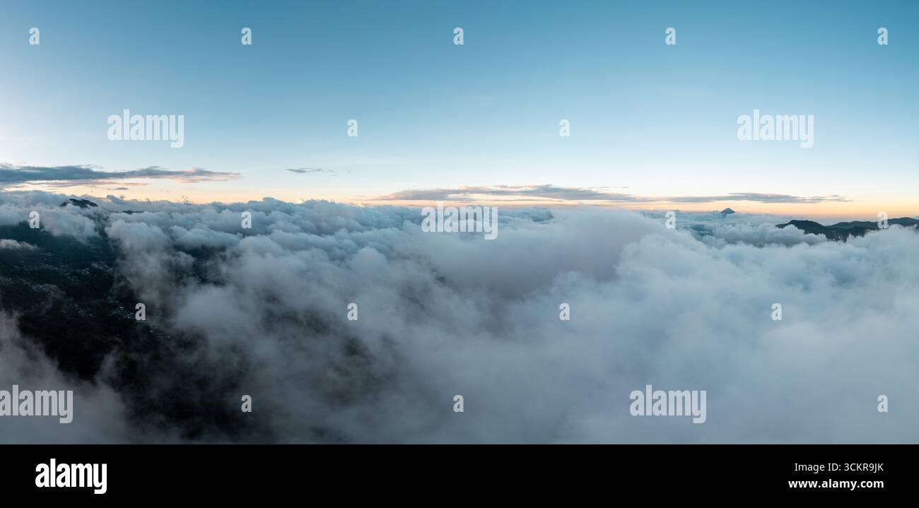 Vista aerea sopra le nuvole al tramonto, con luce dorata che illumina gli strati bianchi e grigi, creando un'atmosfera serena e tranquilla Foto Stock