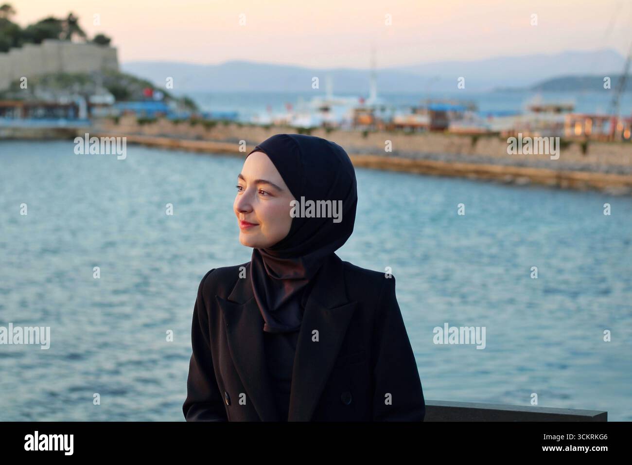 Ritratto di una giovane donna musulmana in hijab sorridente al mare durante il tramonto, che rappresenta diversità, stile di vita, viaggi e cultura. Foto Stock