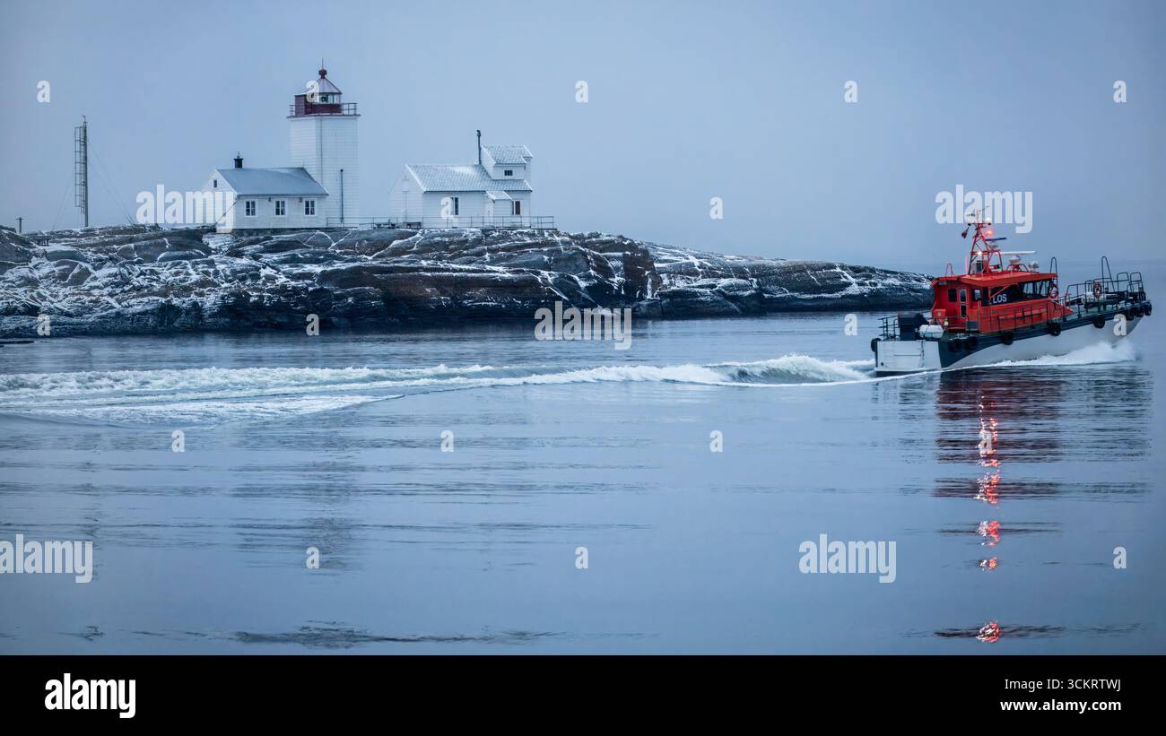 Resistenza artica al faro di Langesund, dove un pilota rosso si sposta attraverso le acque ghiacciate invernali, guidando le navi accanto a rocce innevate e fagioli Foto Stock