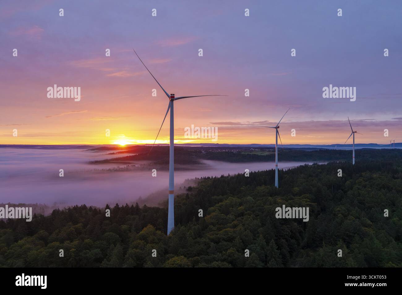 Le turbine eoliche si innalzano sopra una foresta nebbiosa illuminata da un'impressionante alba, vicino a Schorndorf, Remstal, Rems-Murr-Kreis, Baden-Wuerttemberg, Ger Foto Stock