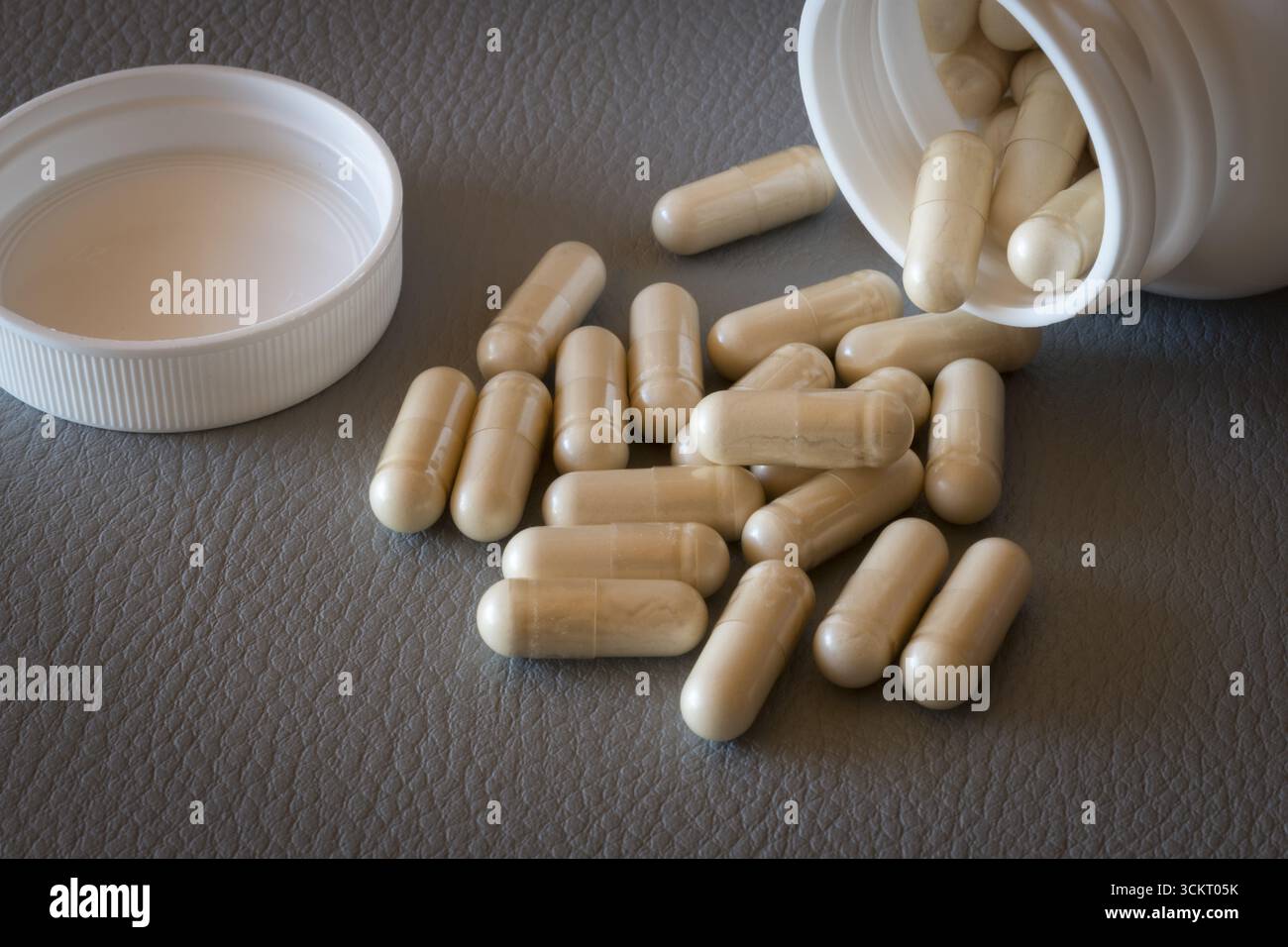 Capsule beige cadute da una bottiglia aperta con il coperchio rimosso su una superficie, integratore alimentare, integratore di ferro, integratore vitaminico Foto Stock