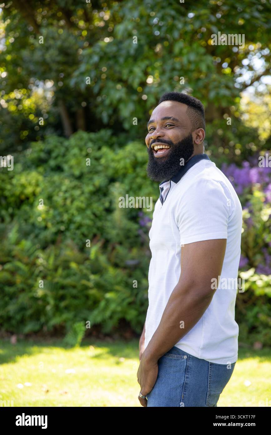 Uomo afro-americano che rideva di cuore, in piedi leggermente girato a sinistra in un parco illuminato dal sole, spazio fotocopie Foto Stock