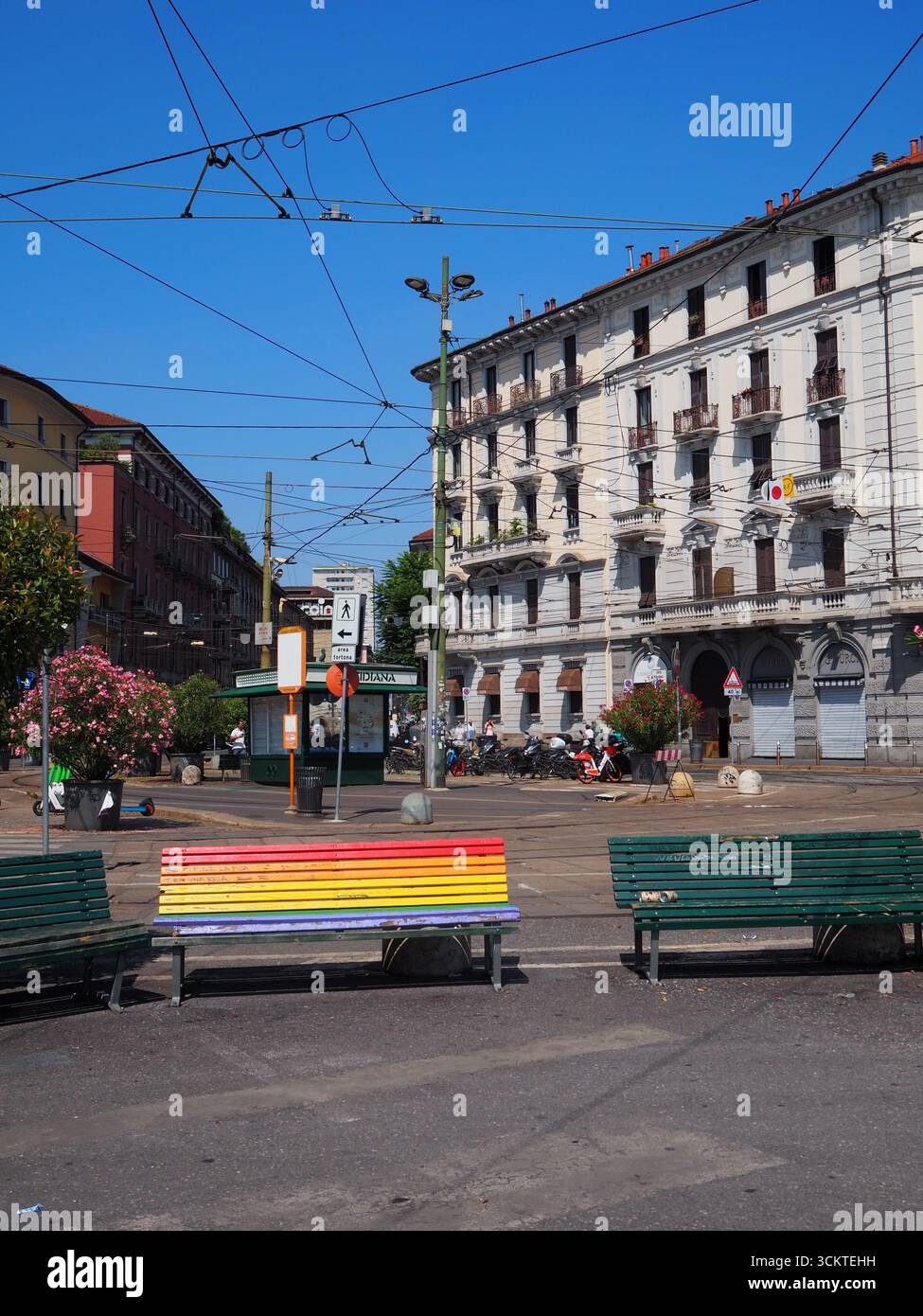 Panchina arcobaleno di fronte alla stazione di Milano porta Genova con edifici storici e cavi del tram nel quartiere dei Navigli Foto Stock