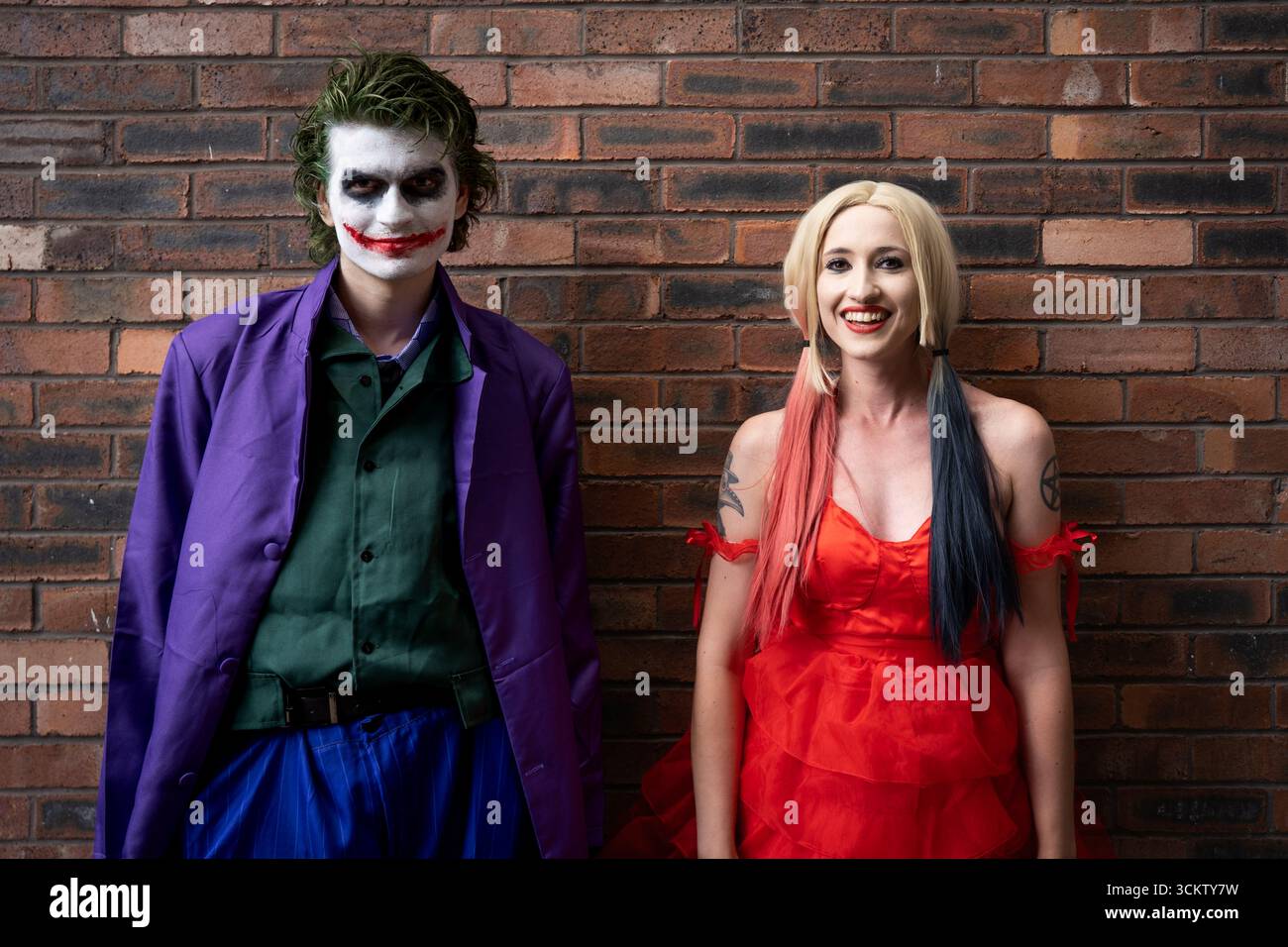 Una bella ragazza e un bel cosplayer maschio che si diverte e ride mentre si vestono da Joker e Harley Quinn con spazio per copiare sopra Foto Stock