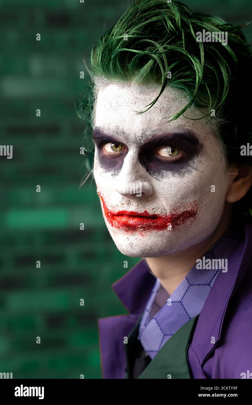 Primo piano ritratto di un giovane cosplayer maschile vestito da Joker con il volto e che guarda direttamente la fotocamera Foto Stock