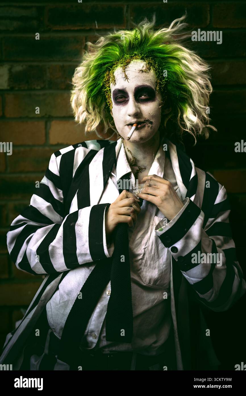 Primo piano ritratto di un giovane cosplayer maschio che ride e si diverte vestito come Beetlejuice con il viso e i capelli verdi Foto Stock