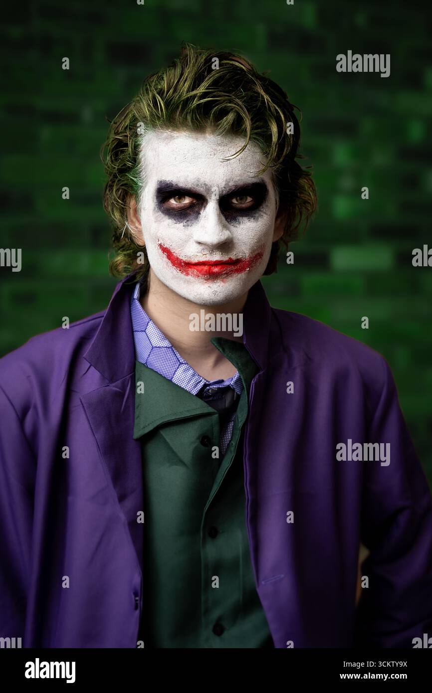 Ritratto di un giovane cosplayer maschile vestito da Joker e divertiti mentre sorridi e guarda direttamente la fotocamera con spazio di copia Foto Stock
