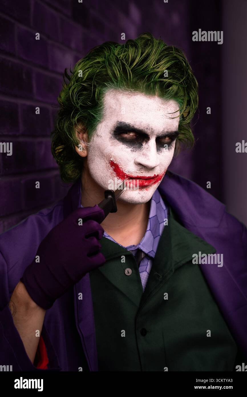Primo piano ritratto di un giovane cosplayer maschile vestito come il Joker con un coltello e sorriso che sembra serio e direttamente alla fotocamera con spazio per le copie Foto Stock